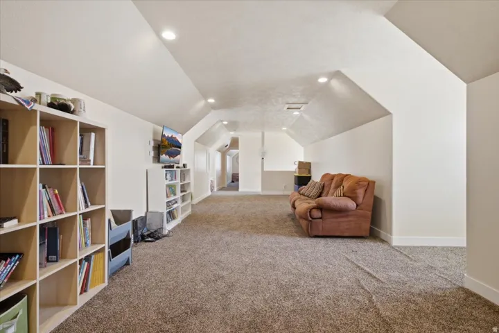 Spacious room featuring vaulted ceilings, recessed lighting, neutral-toned carpet flooring, white painted walls, and built-in shelving