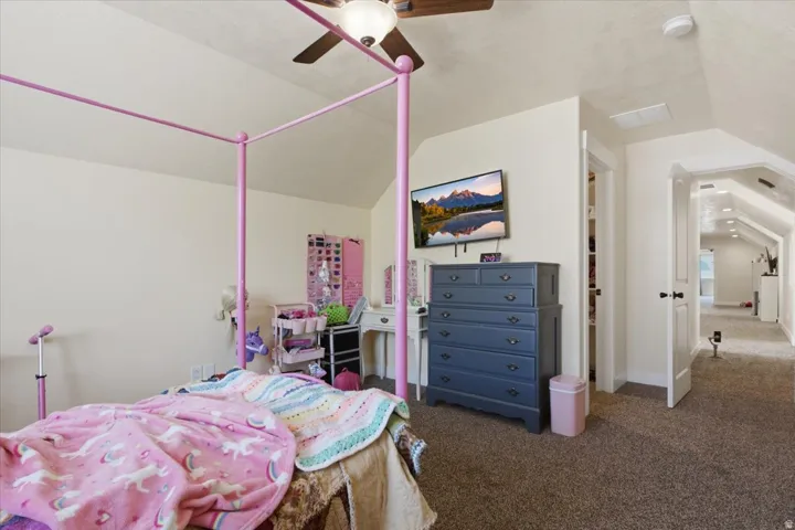 Carpeted room with a ceiling fan, sloped ceilings, and white trim