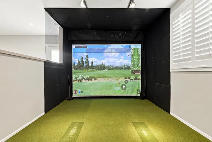 Dedicated golf simulation area featuring a large projection screen, track lighting, green turf flooring, and sound-absorbing wall panels