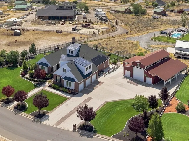 Expansive property featuring a meticulously landscaped front lawn, a large paved driveway, a multi-car garage with an attached carport, and a substantial red barn structure
