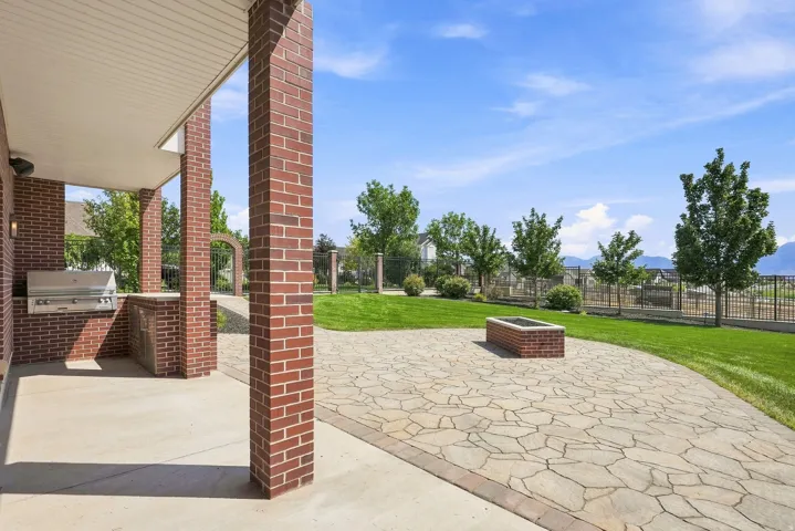 Covered patio featuring an integrated stainless steel grill with a brick surround, ample concrete flooring, and brick columns
