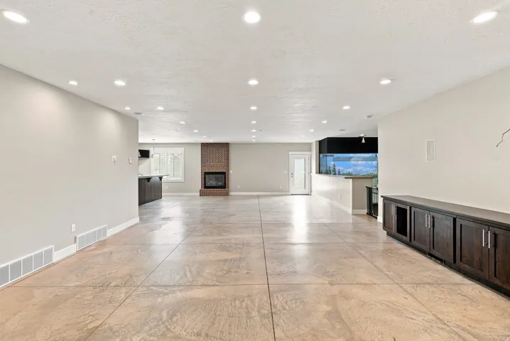 Expansive open-concept living area featuring a brick-surround fireplace, recessed lighting, and large format tile flooring