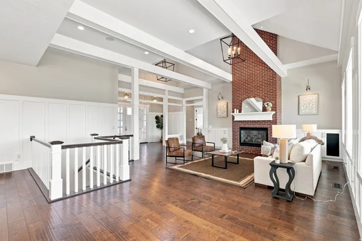 Spacious living area featuring a prominent brick fireplace with a white mantel, high vaulted ceilings with exposed beams, and rich wood-finish flooring