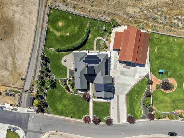 Expansive property featuring a main residence with solar panels, a substantial detached outbuilding with a red tile roof, and extensive green lawns