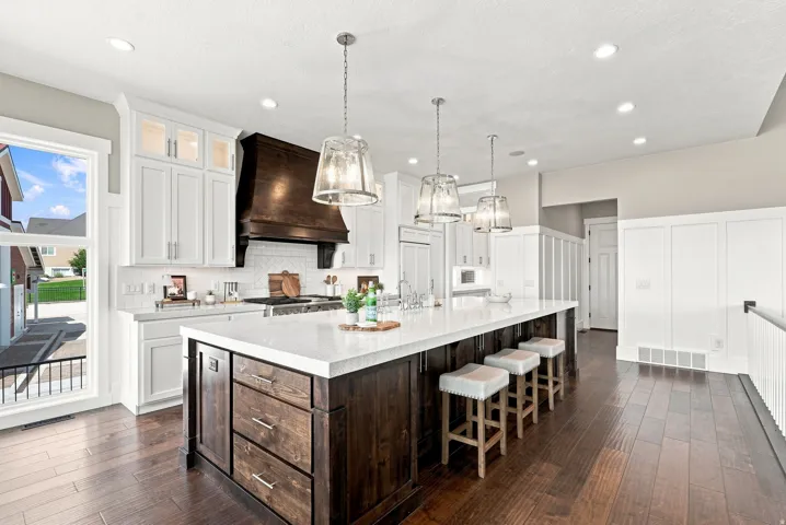Gourmet kitchen featuring a large central island with seating, white shaker cabinetry, a rich wood-finish range hood, stainless steel appliances, and wood-finish flooring