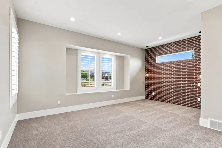 Spacious room with a decorative brick accent wall, recessed lighting, and a large window with white plantation shutters