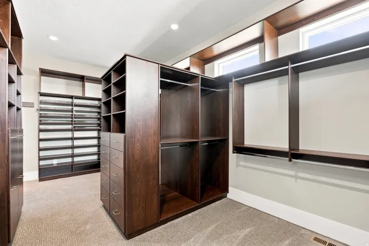 Custom closet system featuring dark wood-finish cabinetry, extensive shelving, built-in drawers, hanging rods, and recessed lighting
