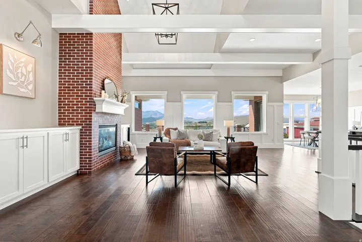 Spacious living area featuring rich wood-finish flooring, a prominent brick fireplace with a white mantel, and white built-in cabinetry