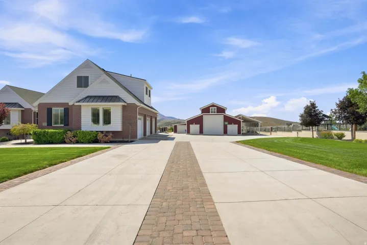 Expansive concrete driveway with a brick paver inlay leading to a brick and siding residence featuring a three-car garage and a separate red barn structure with multiple bays