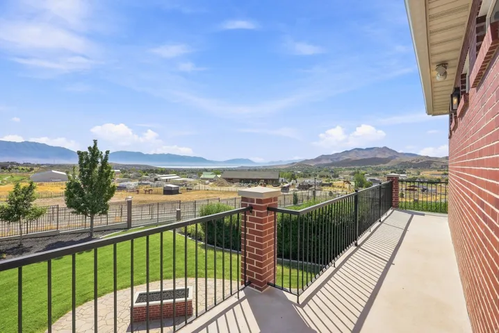 Expansive outdoor balcony with concrete flooring, black metal railings, and brick pillars