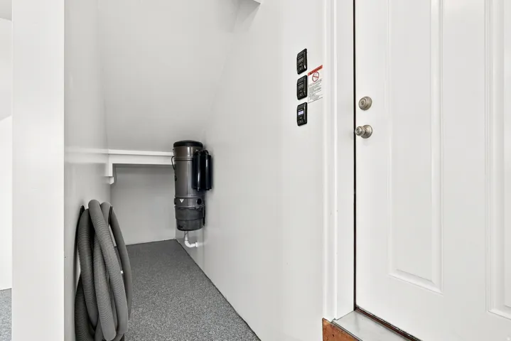 Under-stair storage area featuring a central vacuum system, wall-mounted controls, and durable speckled flooring