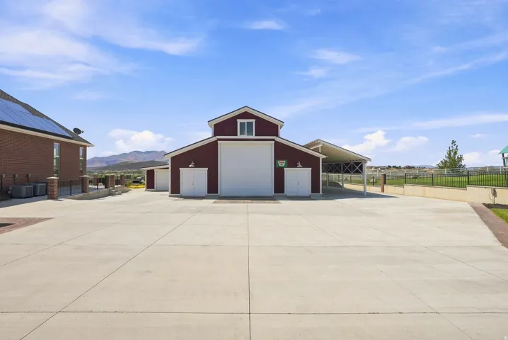Expansive concrete pad serving a red-sided barn-style structure with multiple garage doors and an attached covered carport