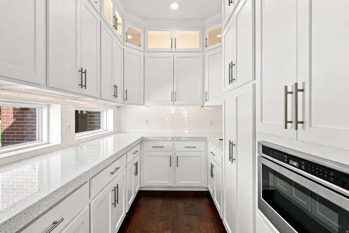 Contemporary galley kitchen featuring white shaker cabinetry, light speckled countertops, a white subway tile backsplash, and dark wood-finish flooring