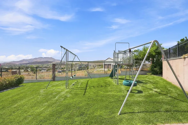 Expansive grassy yard featuring a play structure, swing set, and black metal fencing