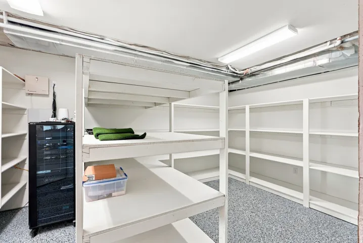 Utility room featuring extensive built-in shelving, durable epoxy flooring, and fluorescent ceiling lighting