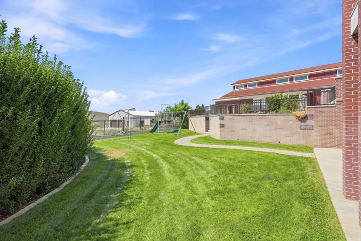 Expansive green space featuring a manicured lawn, established shrubbery, and a paved pathway