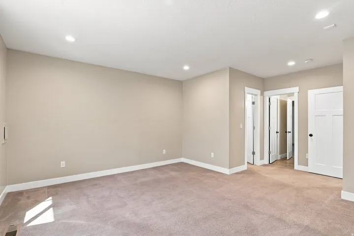 Spacious room featuring neutral wall tones, recessed lighting, plush carpeting, white baseboards, and white interior doors with black hardware