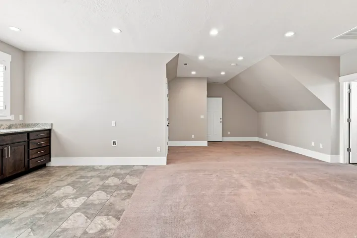 Spacious versatile room featuring recessed lighting, a built-in cabinetry unit with a granite-style countertop, and a mix of patterned tile and carpet flooring