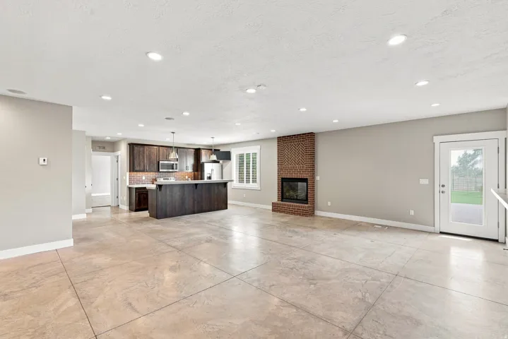 Spacious room featuring concrete flooring, a brick fireplace, a kitchen island with pendant lighting, dark wood-finish cabinetry, and recessed lighting