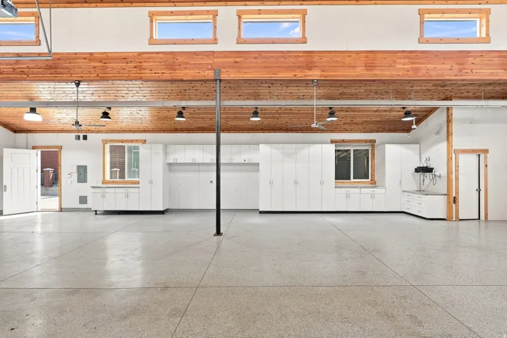 Spacious utility area featuring extensive white cabinetry, durable concrete flooring, exposed wood beam ceiling, multiple ceiling fans, and task lighting