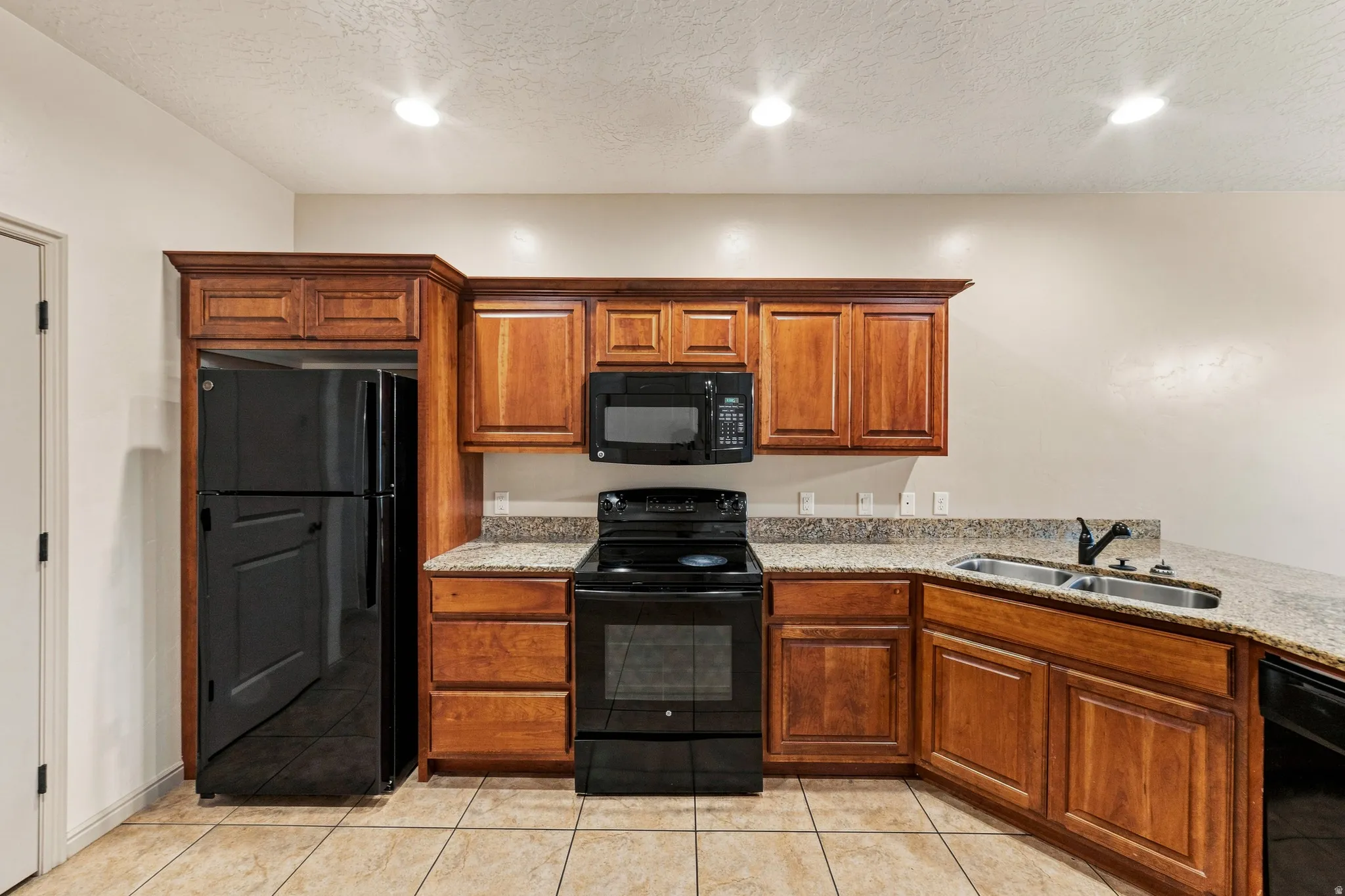 Kitchen featuring wood cabinetry, granite-look countertops, black appliances, a double basin sink with a matte black faucet, and recessed ceiling lighting