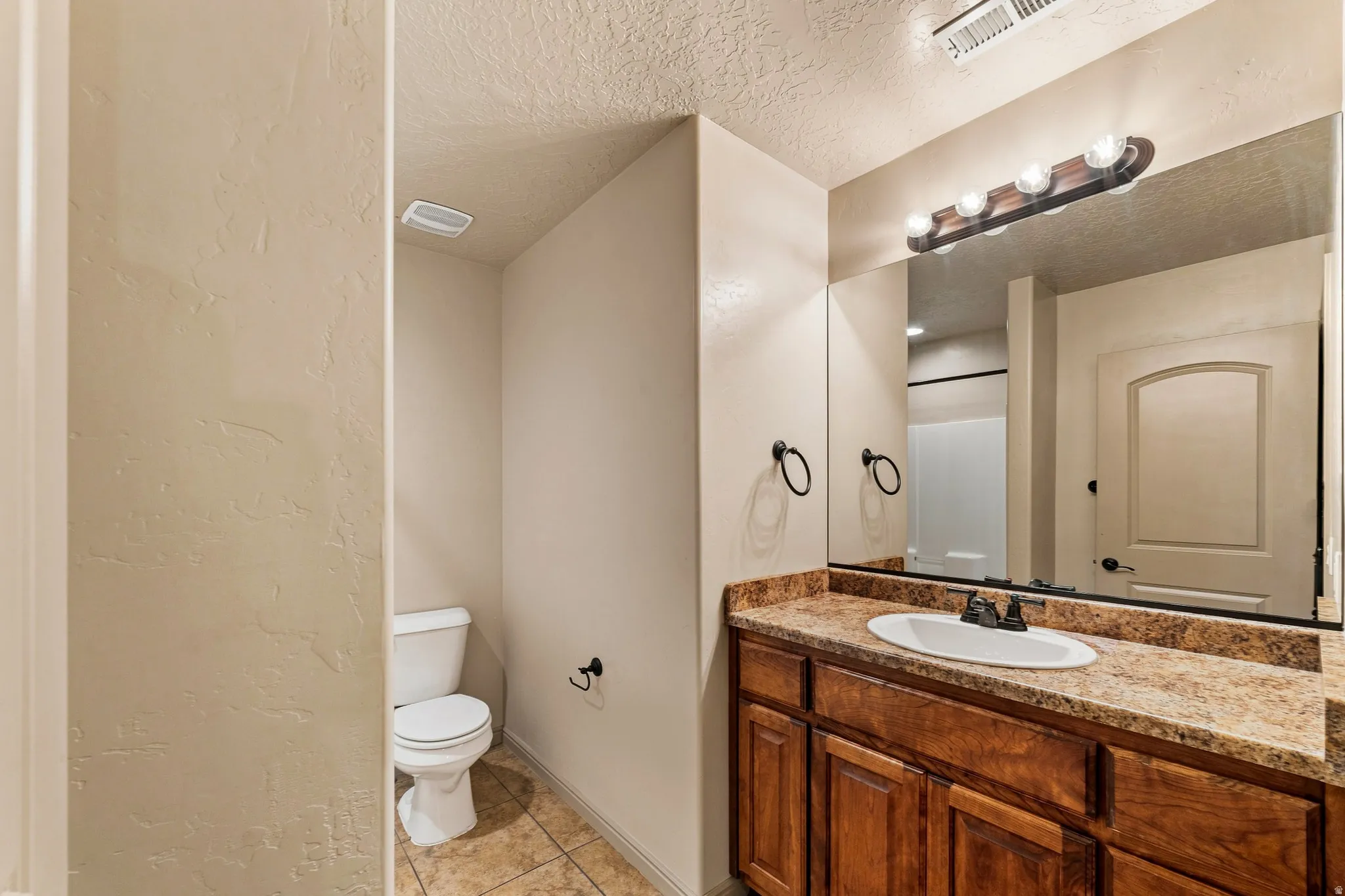Bathroom featuring a wood-finish vanity with a speckled countertop, an integrated sink, and a wall-mounted mirror with a five-bulb light fixture