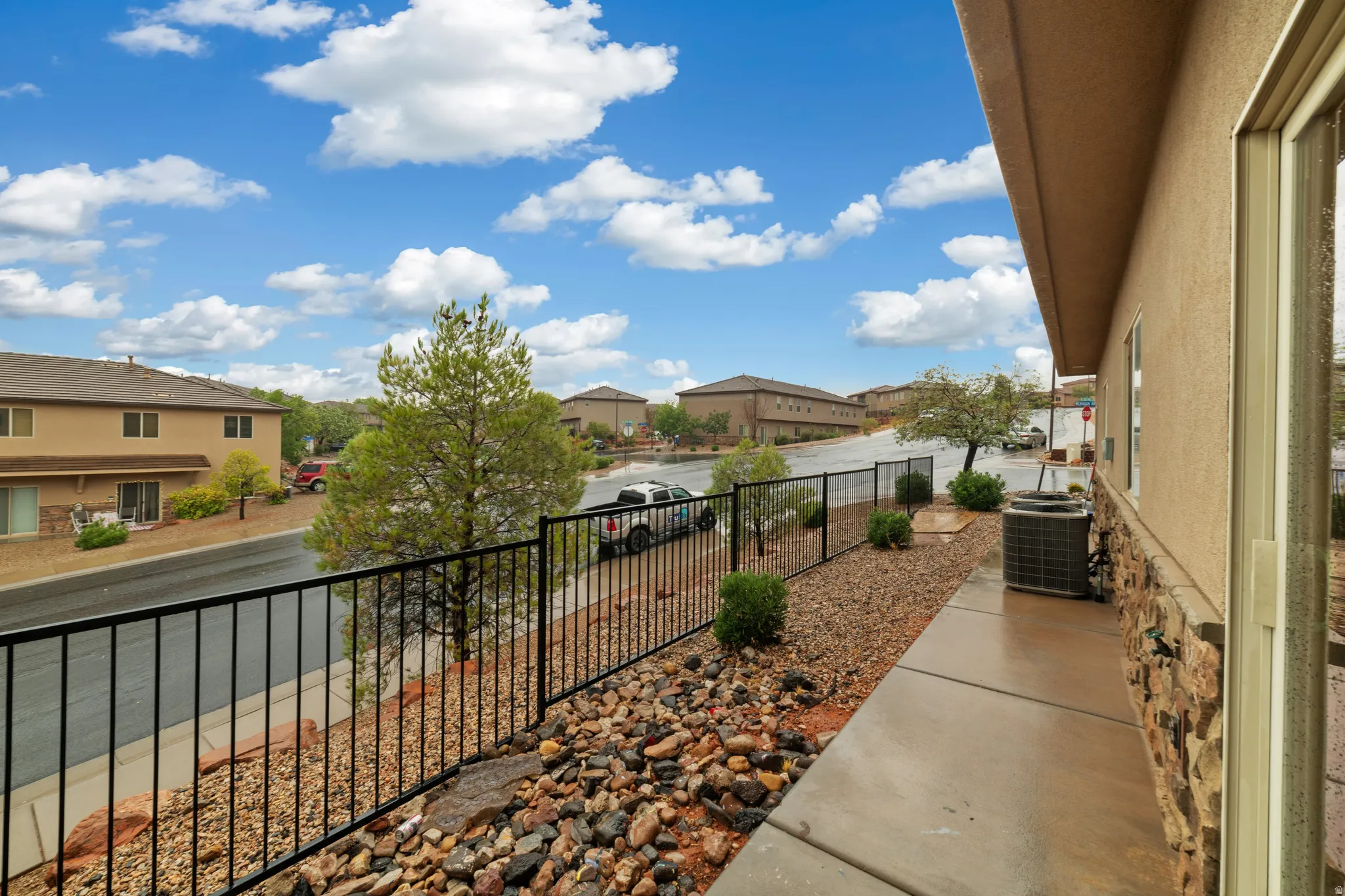 Stucco exterior featuring stone veneer siding, a concrete walkway, and a black wrought iron fence
