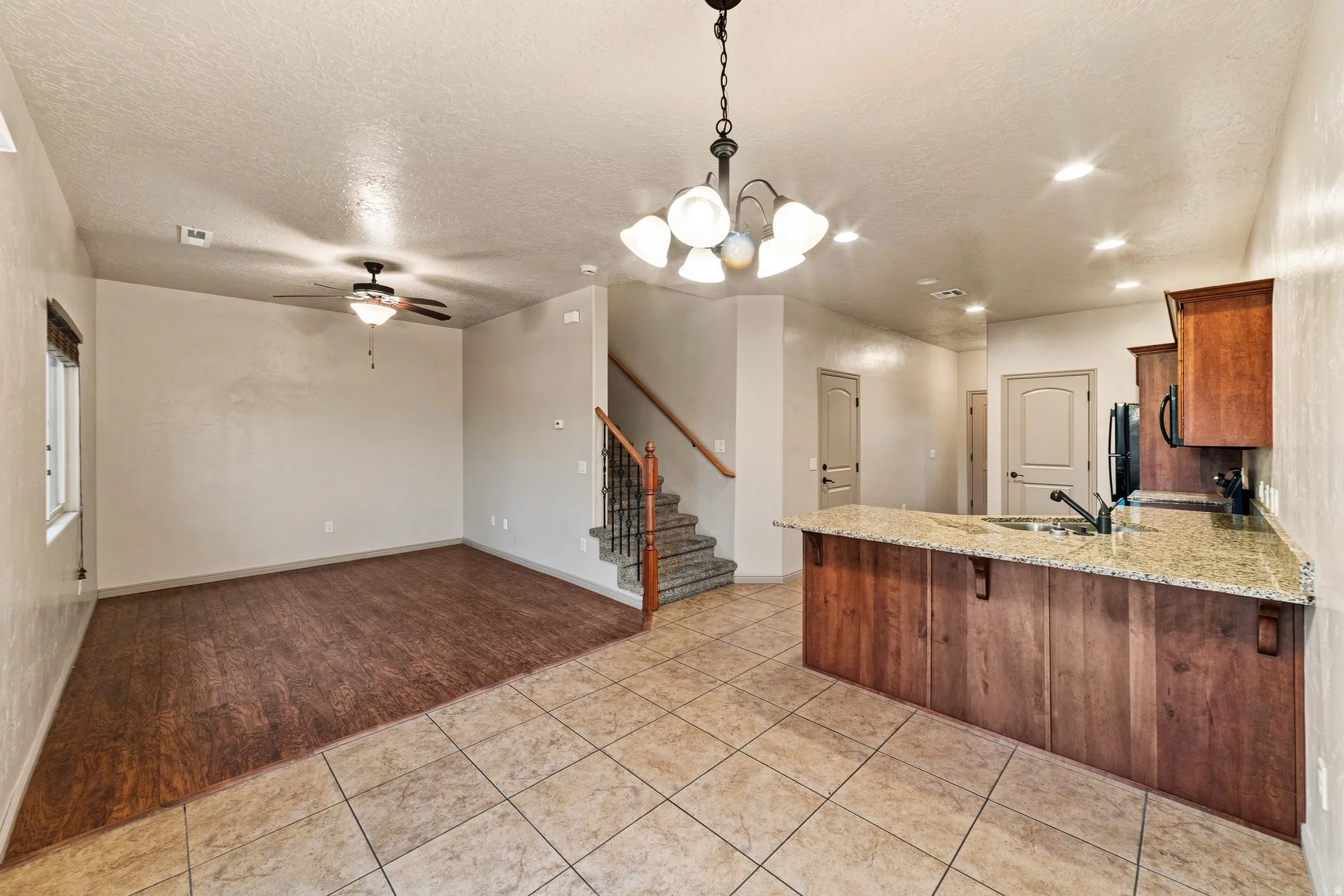 Open-concept living area featuring wood-finish flooring, a ceiling fan with integrated lighting, and a staircase with wood handrails and wrought iron balusters