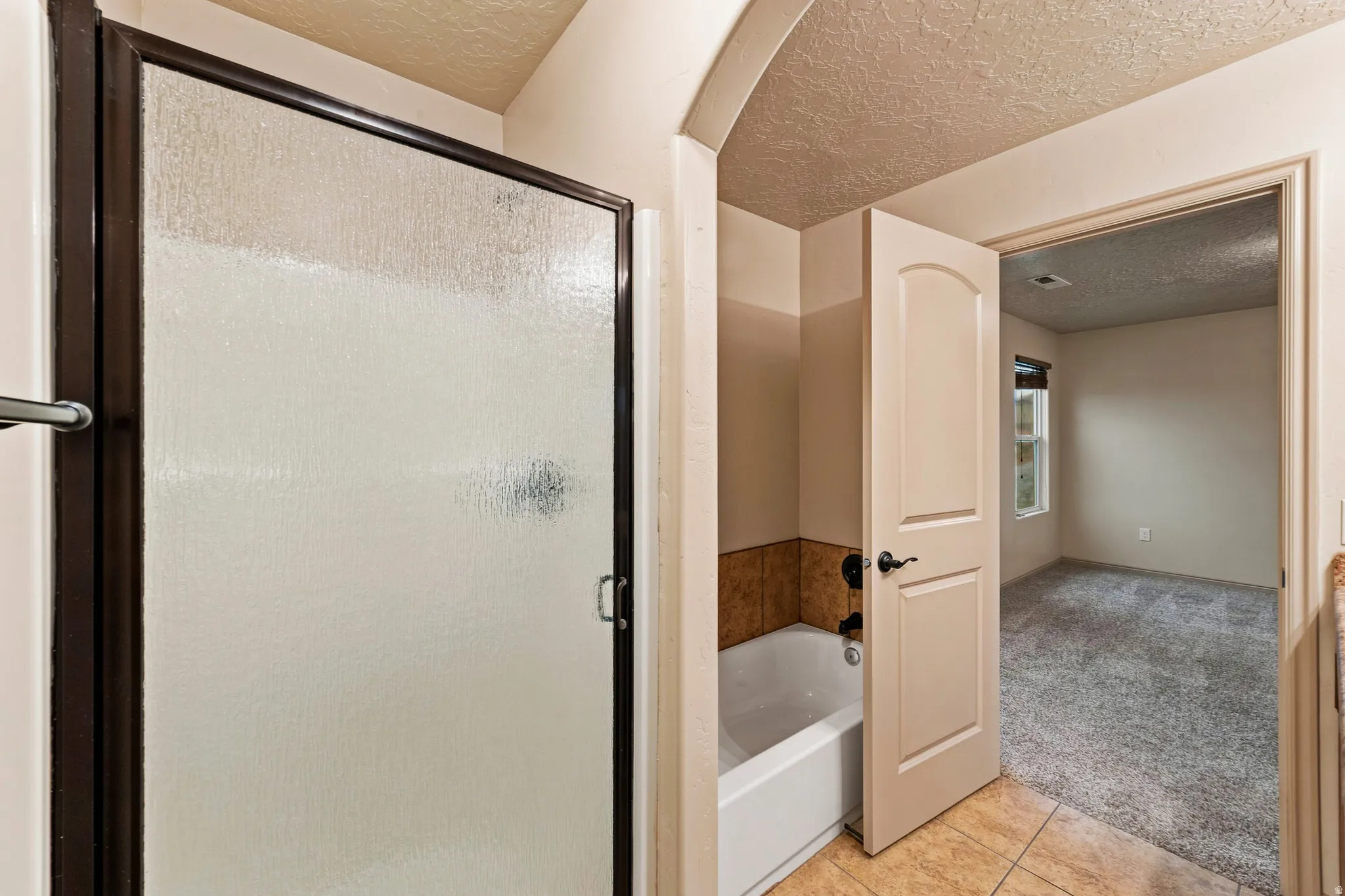 Bathroom featuring a shower with a frosted glass enclosure and dark frame, a bathtub with tile surround, and a light-colored arched panel door