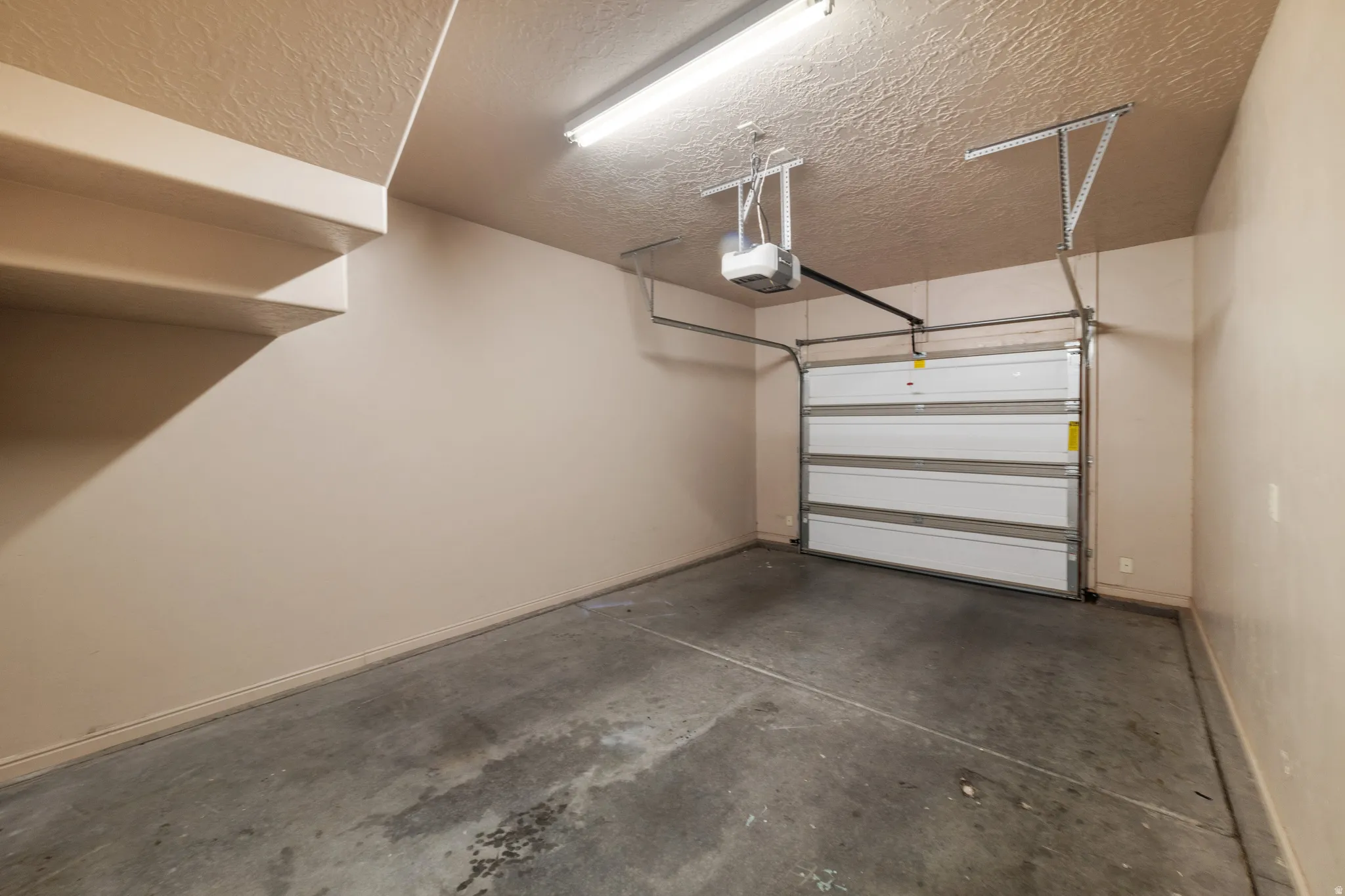Single-bay garage with a concrete floor, automatic garage door opener, and overhead fluorescent lighting