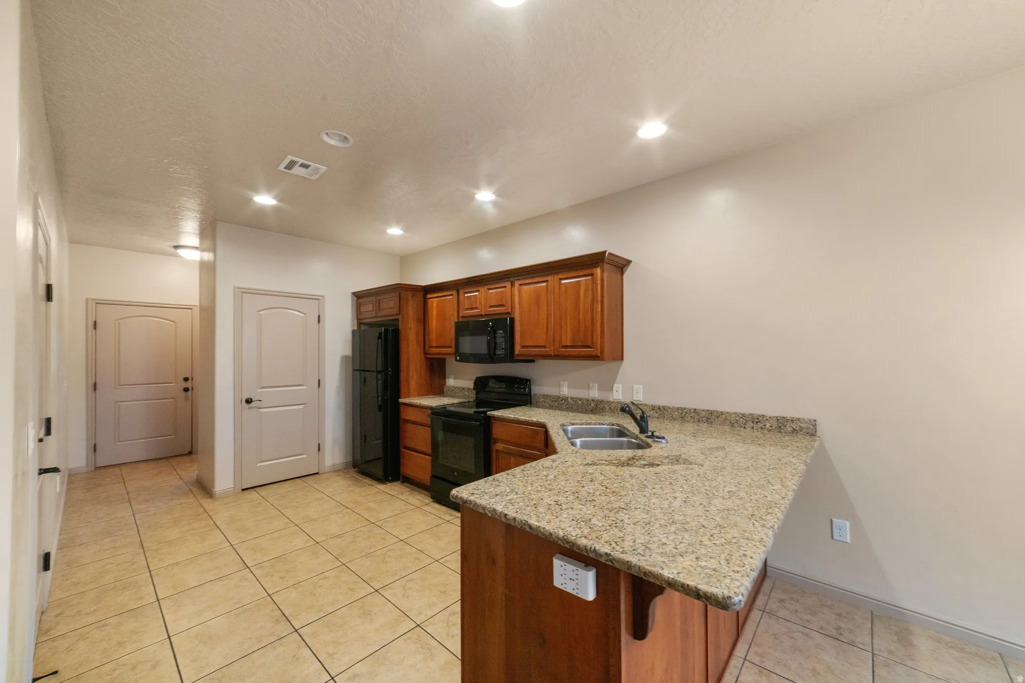 Kitchen featuring wood cabinetry, black appliances, a double basin sink, and a speckled countertop with a breakfast bar
