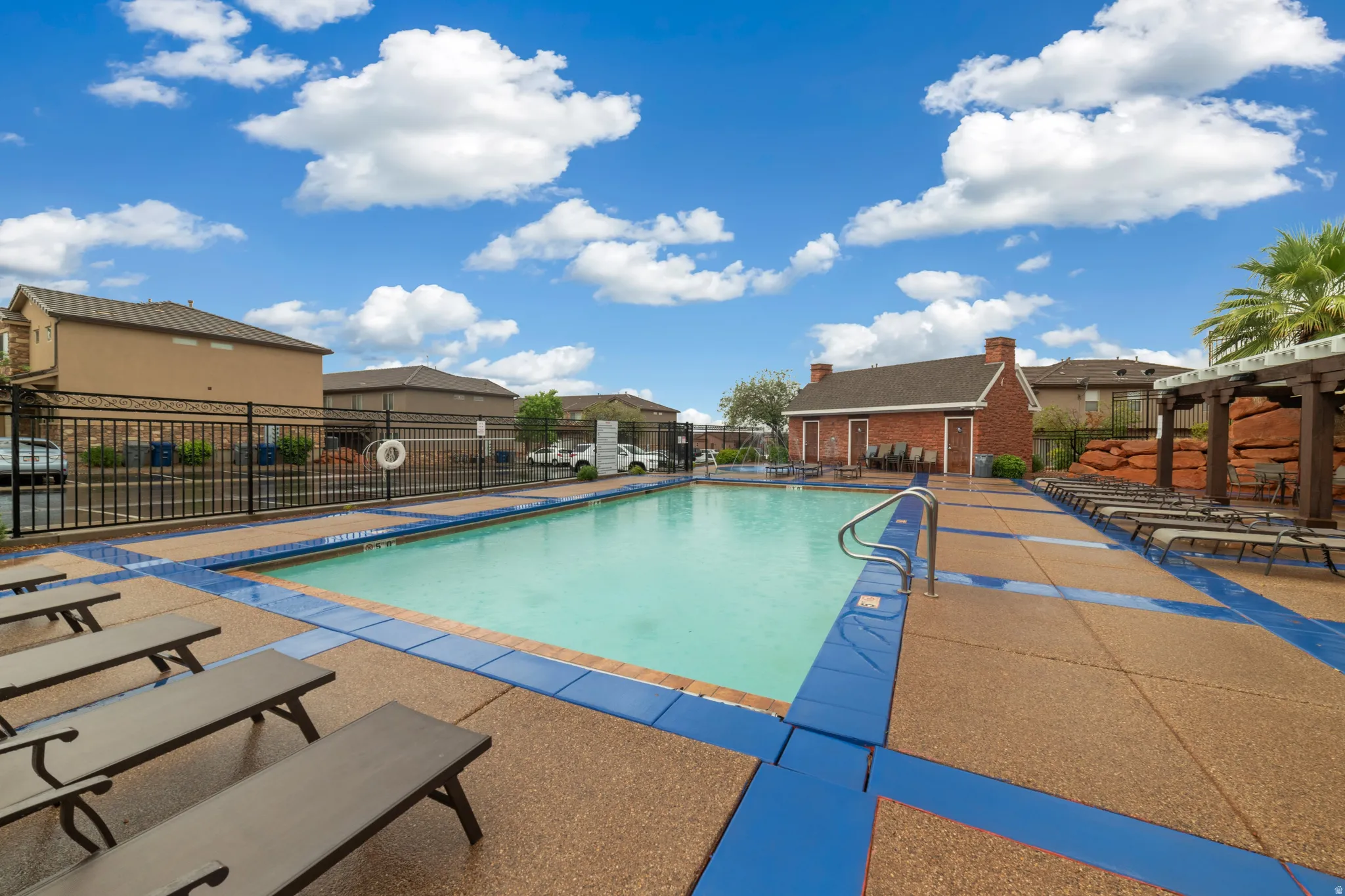 Resort-style swimming pool with integrated steps, surrounded by a textured concrete deck and perimeter fencing