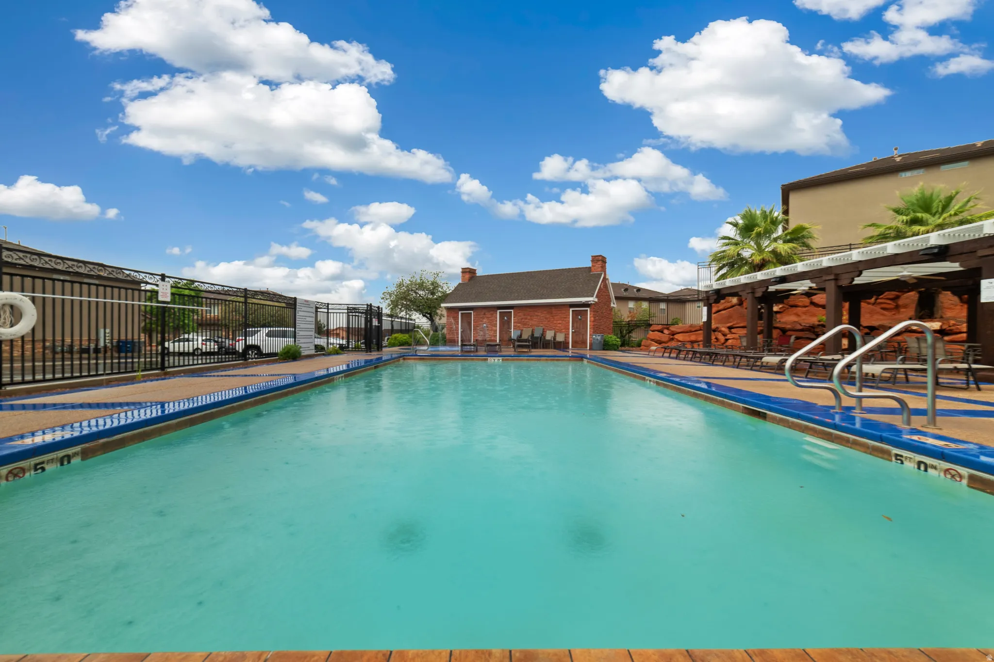 Expansive outdoor swimming pool featuring a perimeter fence, a brown coping, and blue waterline tiles