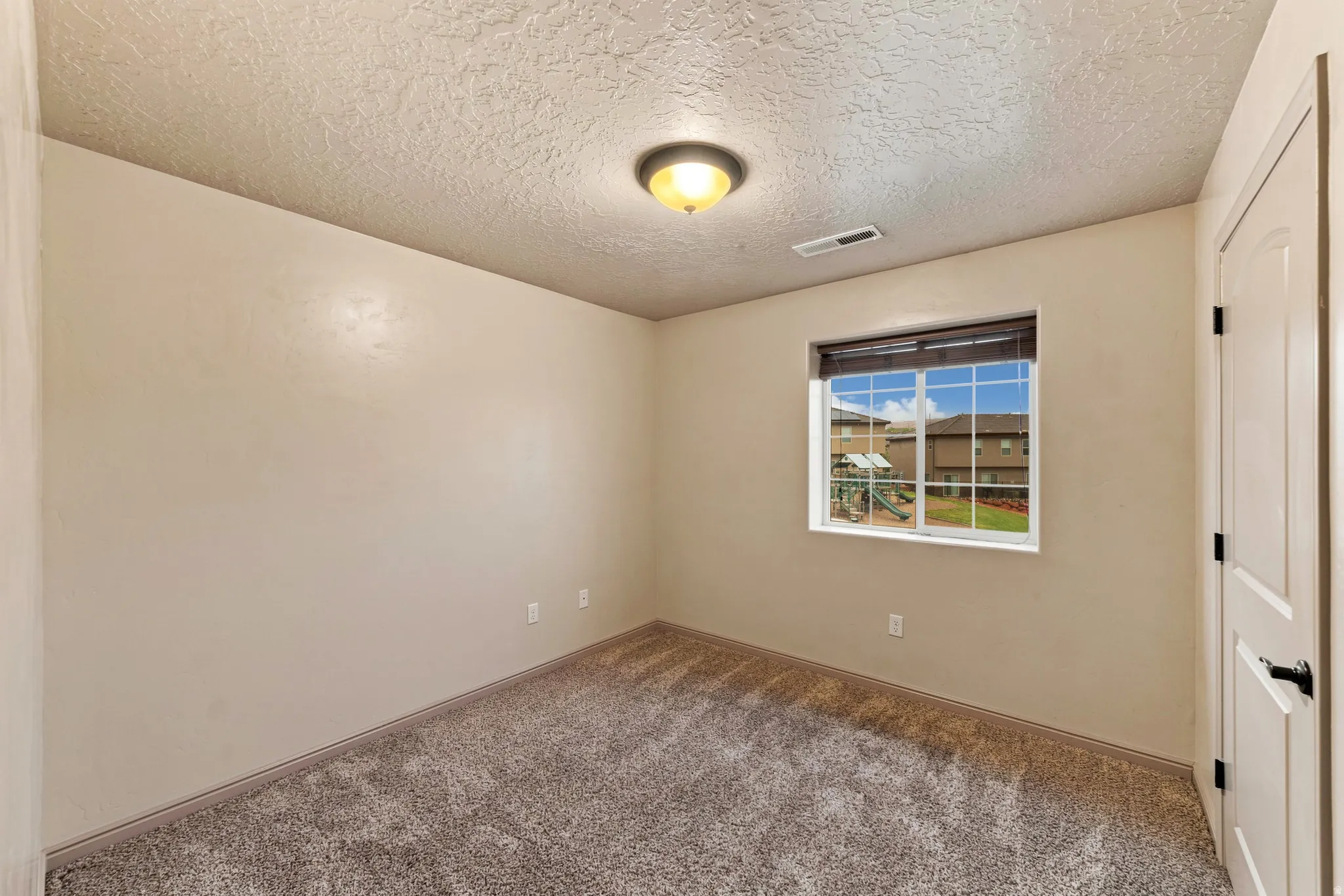 Neutral-toned room featuring textured carpeting and a single window with blinds