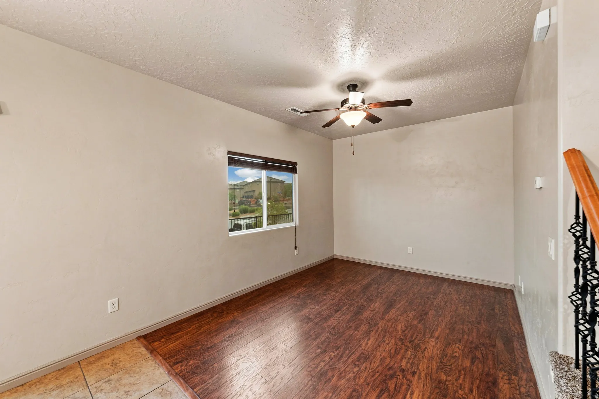 Spacious room featuring wood-finish flooring, a contemporary ceiling fan with light fixture, and a large window providing outdoor scenery