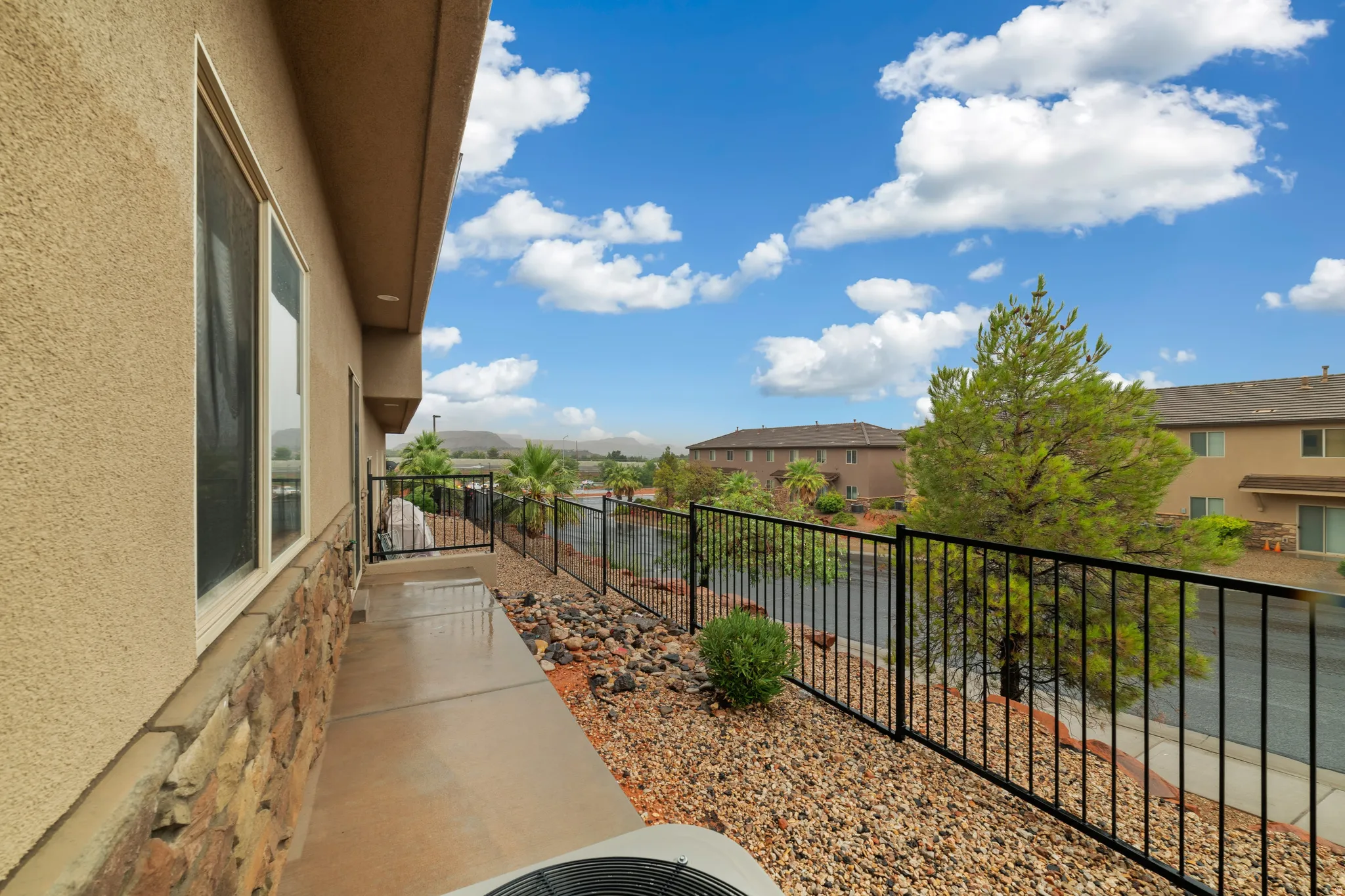 Exterior balcony featuring a concrete surface, decorative rock landscaping, and a black wrought iron fence