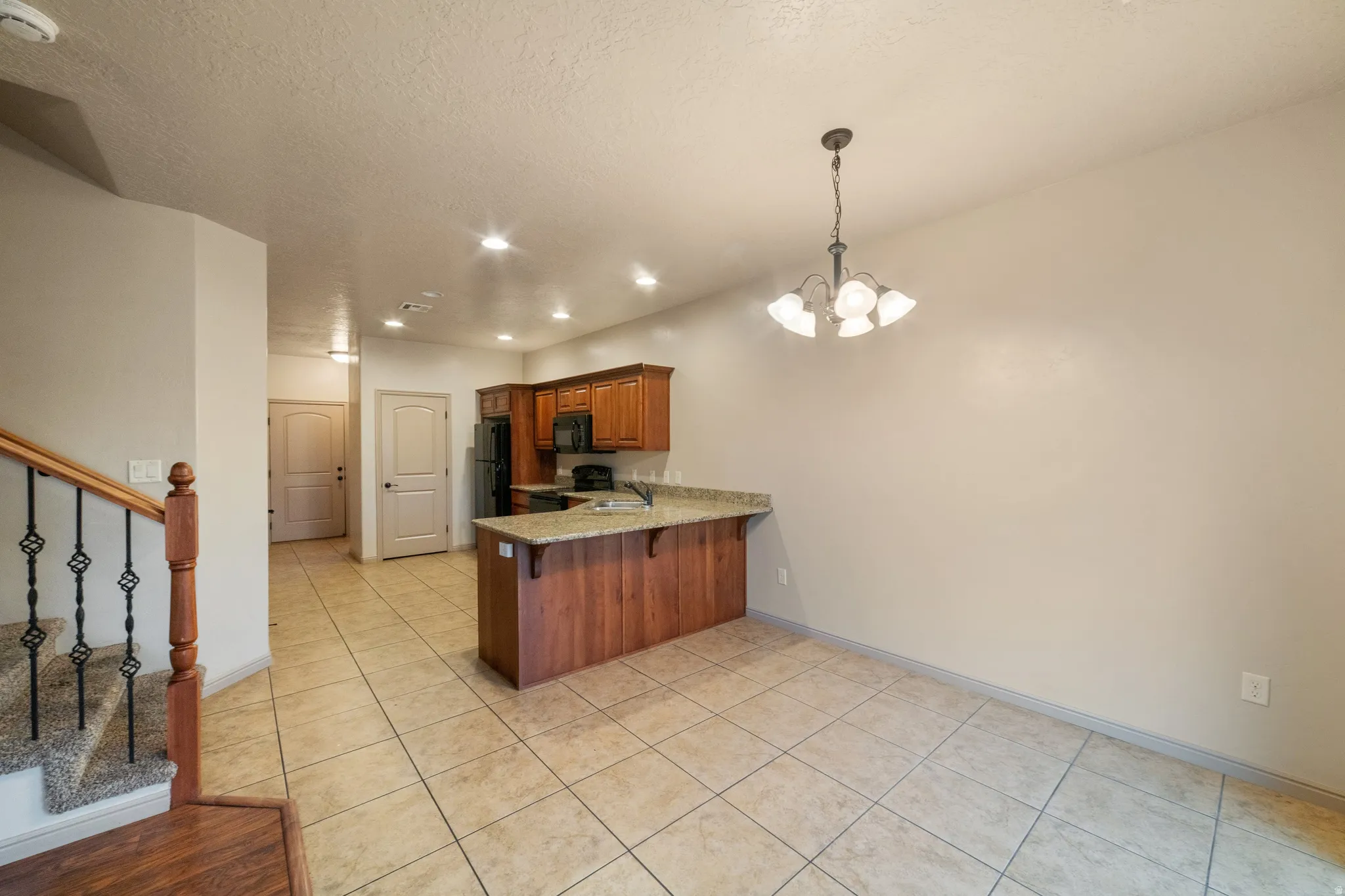 Open-concept living area featuring a kitchen with wood cabinetry, granite-finish countertops, and black appliances