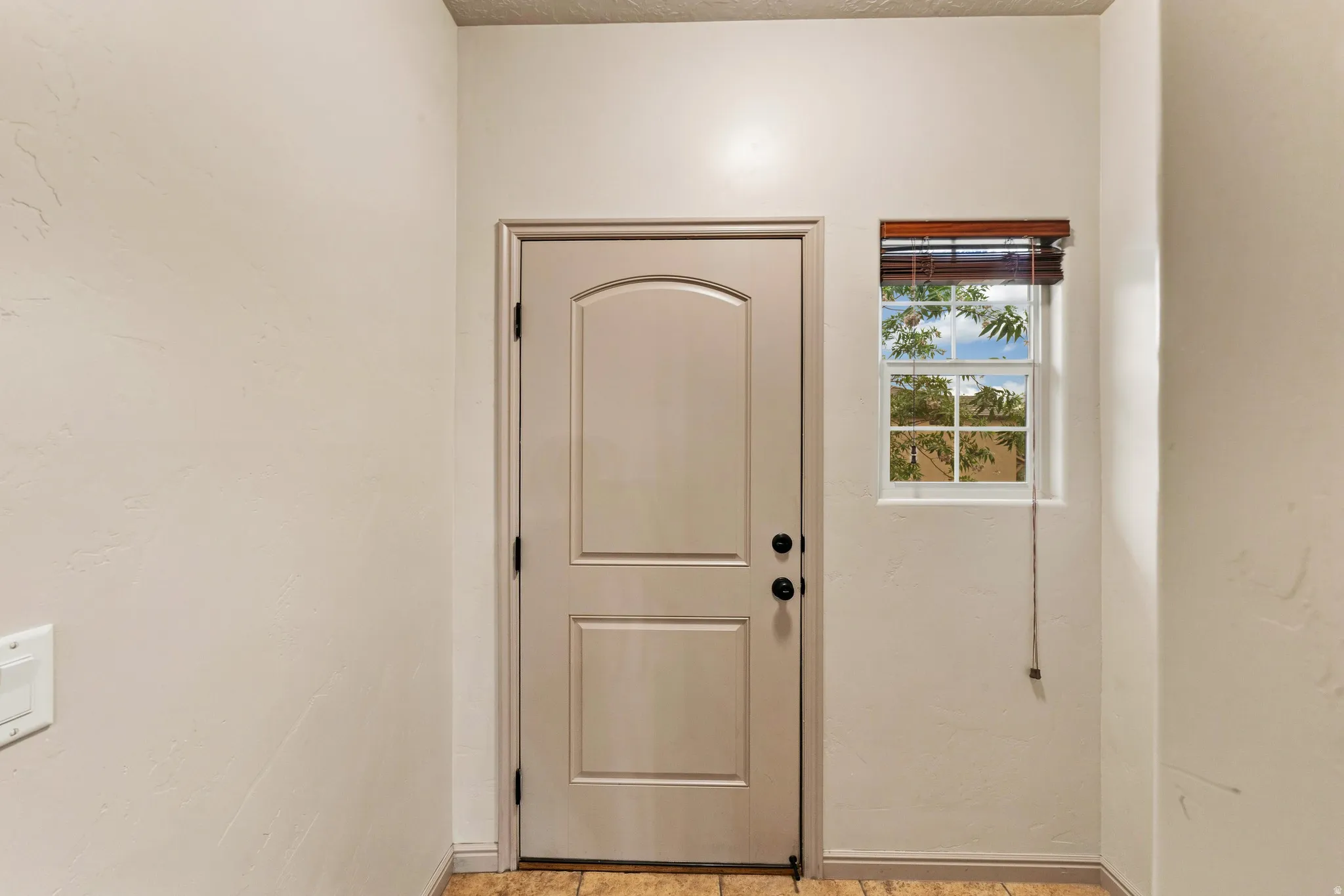 Entry door with arch paneling and black hardware, complemented by a single-pane window with a wood-finish blind