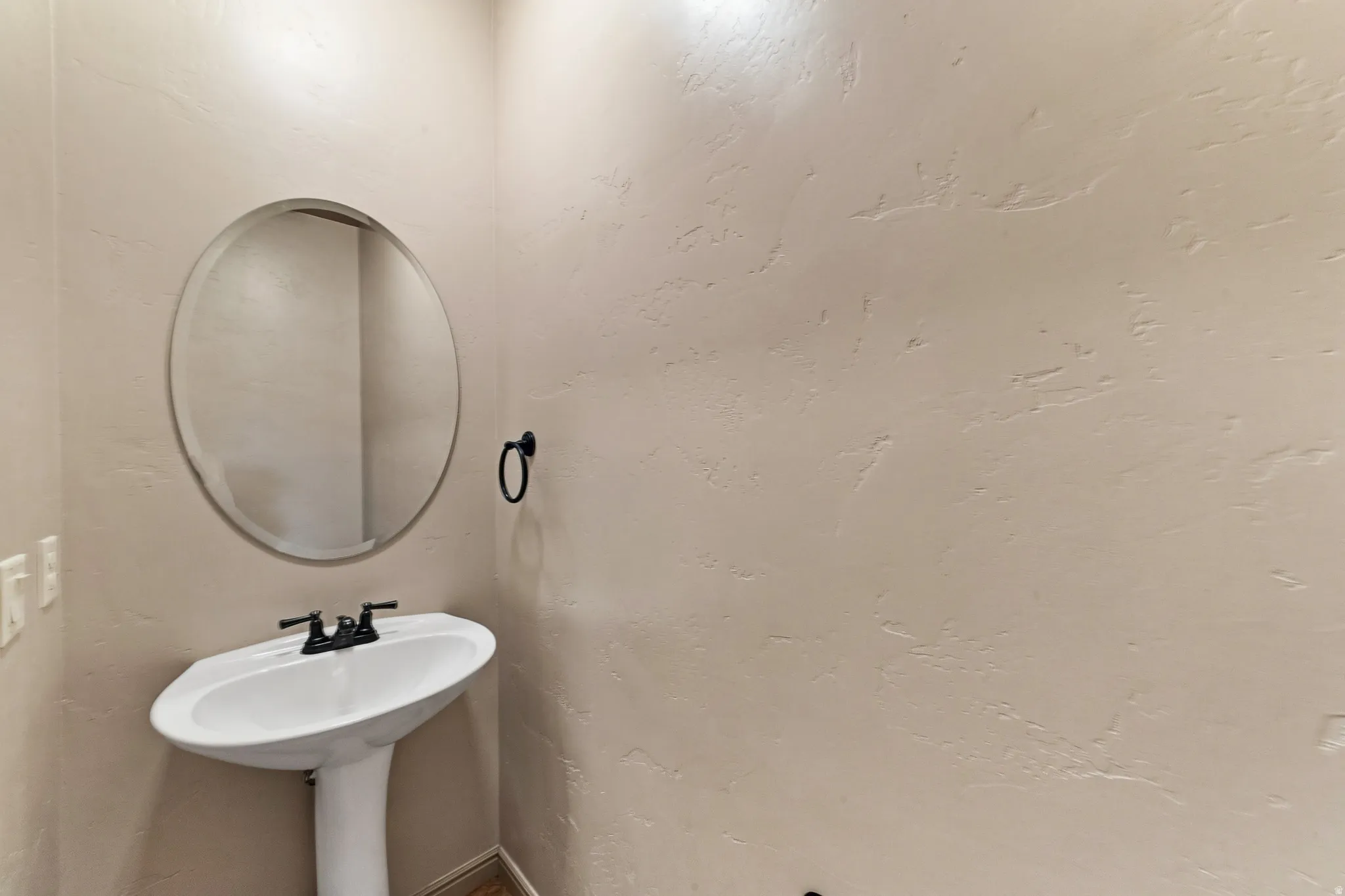 Pedestal sink with dark-finished faucet, illuminated by overhead lighting