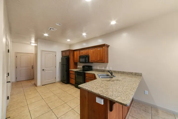 Kitchen featuring wood cabinetry, black appliances, a double basin sink, and a speckled countertop with a breakfast bar