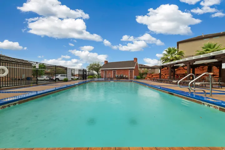 Expansive outdoor swimming pool featuring a perimeter fence, a brown coping, and blue waterline tiles