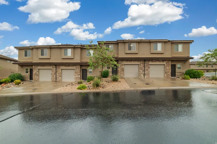 Multi-unit property featuring a stucco exterior with stone accents, individual garages, and multiple windows