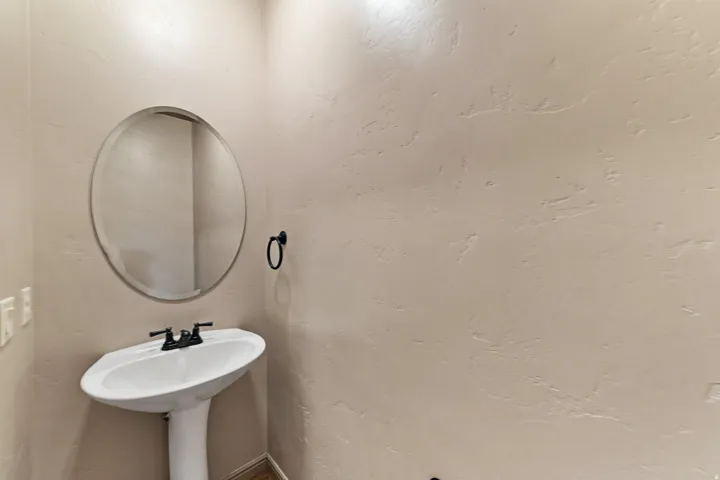 Pedestal sink with dark-finished faucet, illuminated by overhead lighting