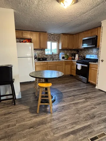 Kitchen featuring wood-finish flooring, natural wood cabinetry, a tiled backsplash, and stainless steel appliances