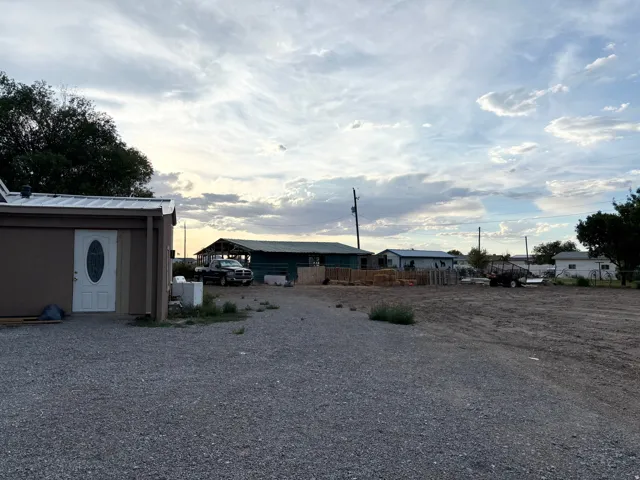 Gravel driveway with an adjacent shed featuring a white door with an oval glass insert and a pitched metal roof