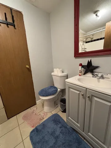 Bathroom featuring a single vanity with a white countertop, a white porcelain toilet, and light-colored tile flooring