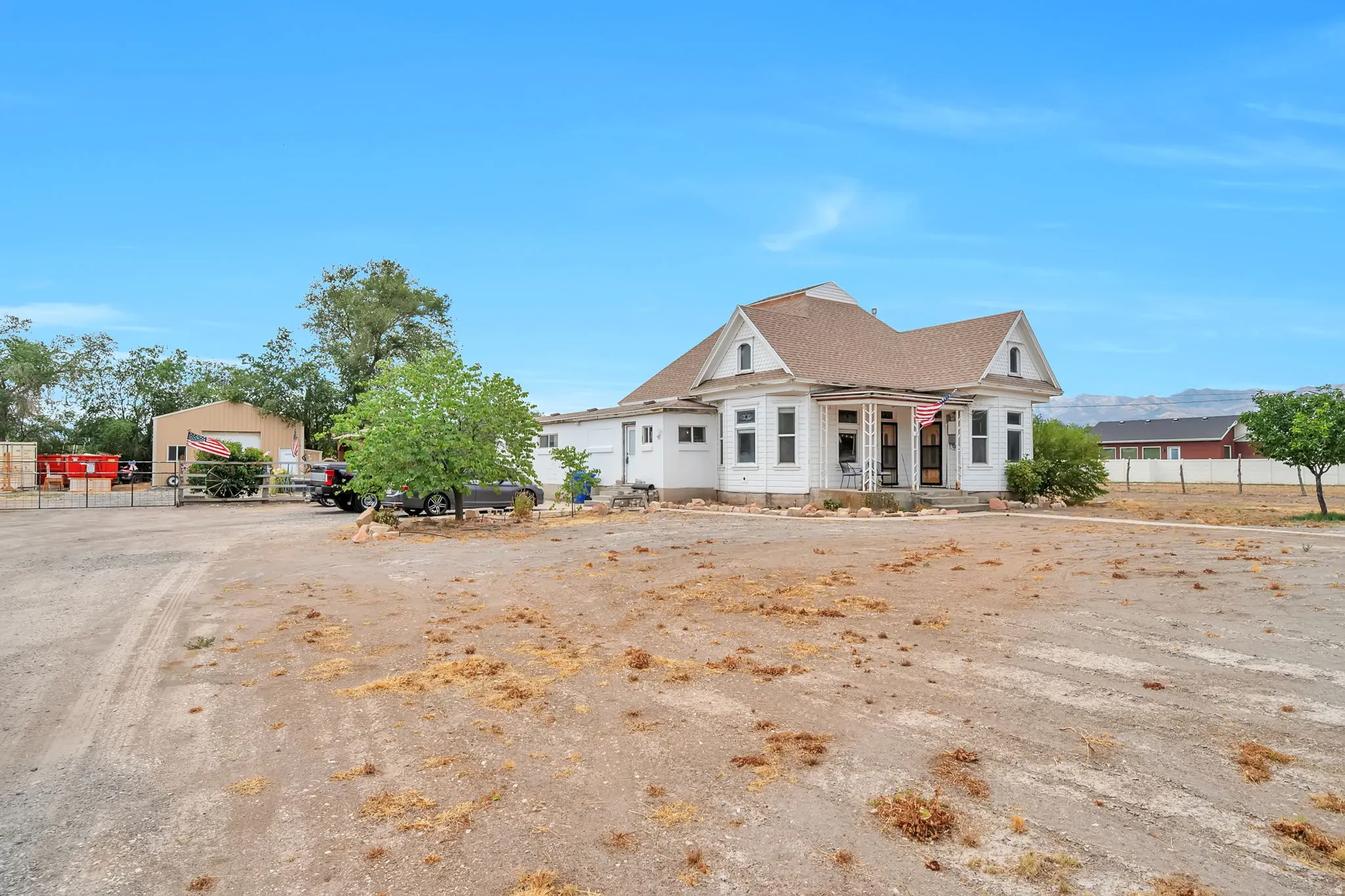 Property exterior featuring a white facade with multiple gabled rooflines, a covered front porch, and an expansive gravel lot