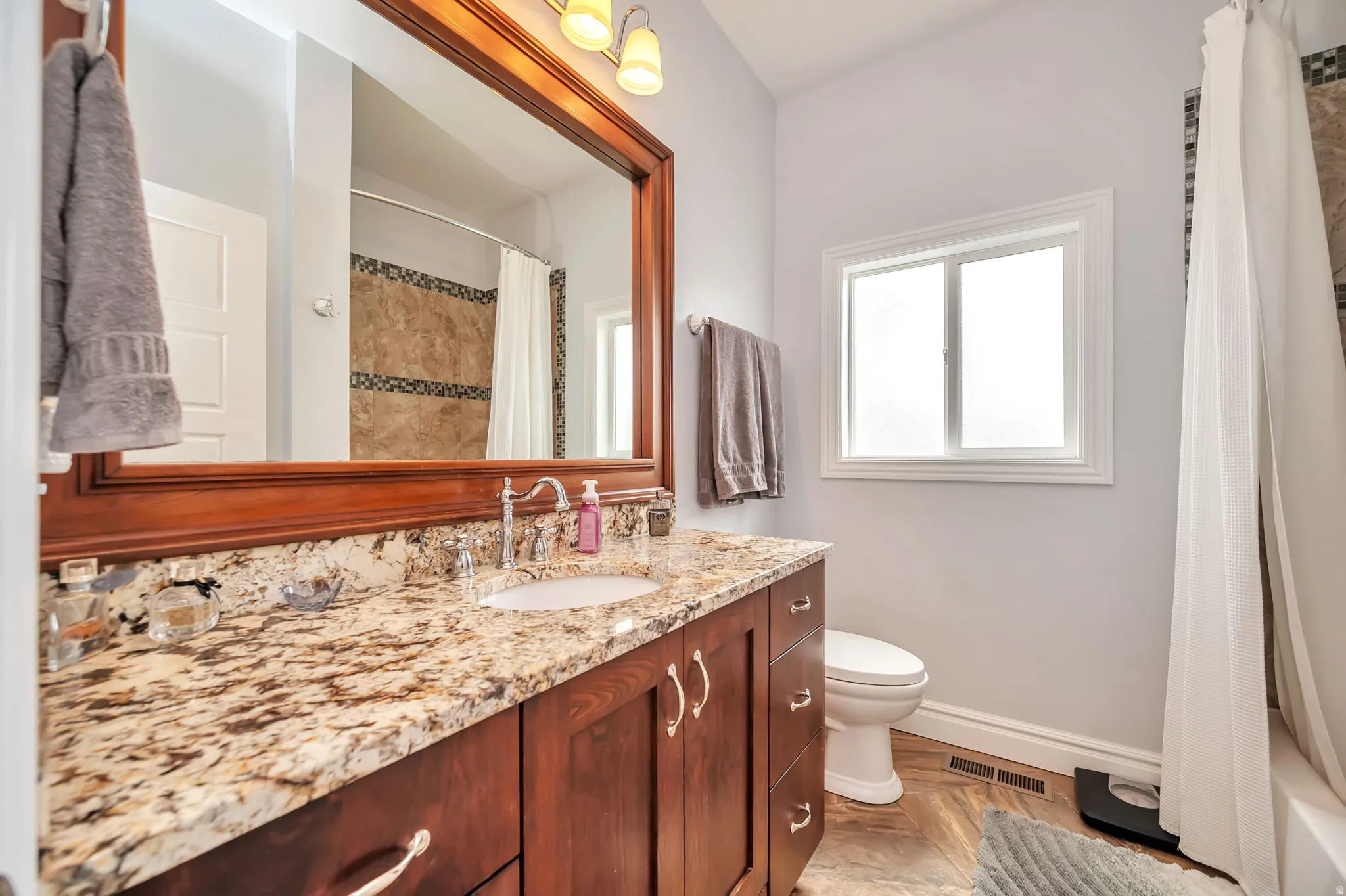 Bathroom featuring a wood vanity with a granite-style countertop, undermount sink, and chrome faucet