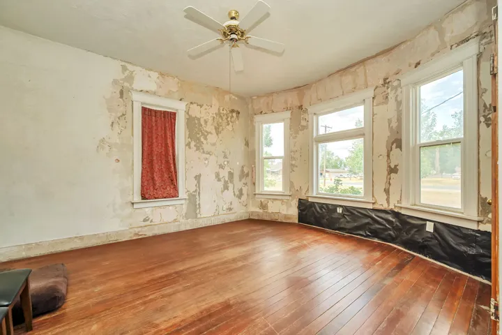 Hardwood flooring throughout a room featuring multiple windows with white trim and a ceiling fan
