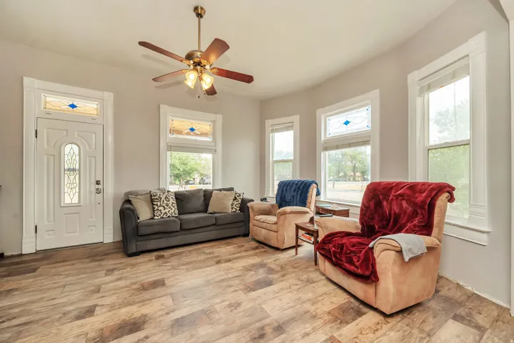 Spacious room featuring wood-finish flooring, a decorative entry door with stained glass, and multiple windows with stained glass transoms